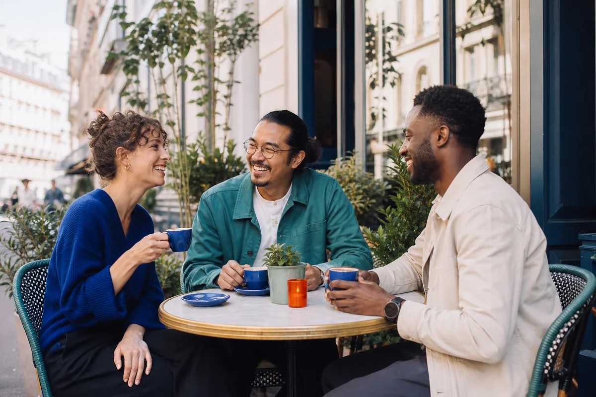 Three friends sharing coffee and conversation on a neighborhood cafe terrace